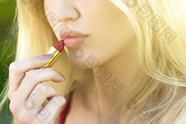 美丽的年轻的金发女郎女人corrects-applying红色的口红化妆公园概念少年生活方式