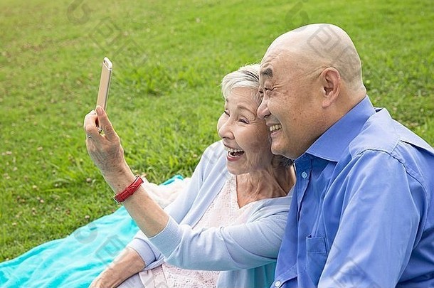 高级夫妇坐着公园采取肖像智能手机