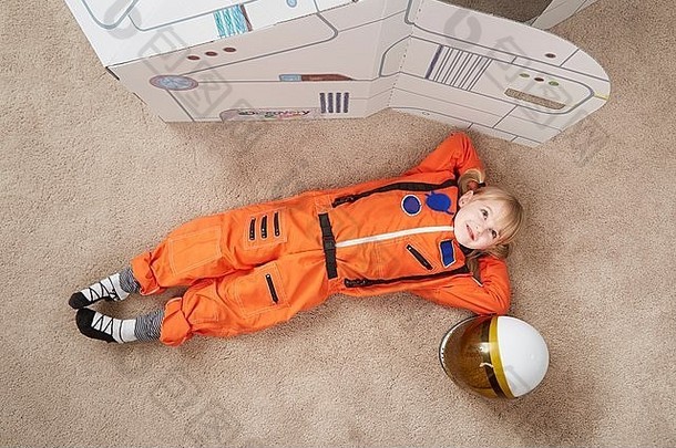 年轻的女孩玩穿宇航员装说谎纸板宇宙飞船升高视图