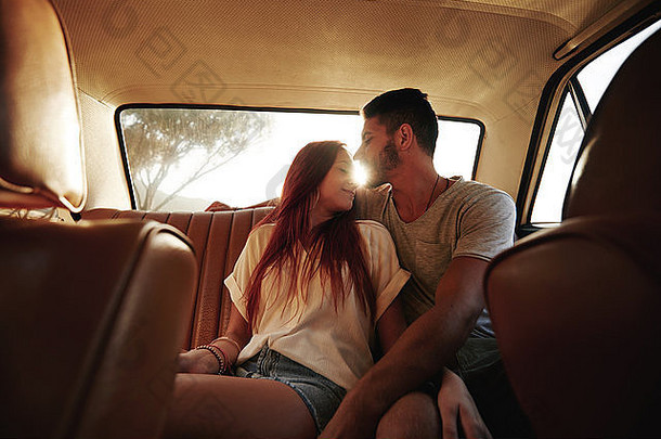 充满深情的年轻的夫妇坐着回来座位车年轻的男人。女人后座位车辆太阳耀斑