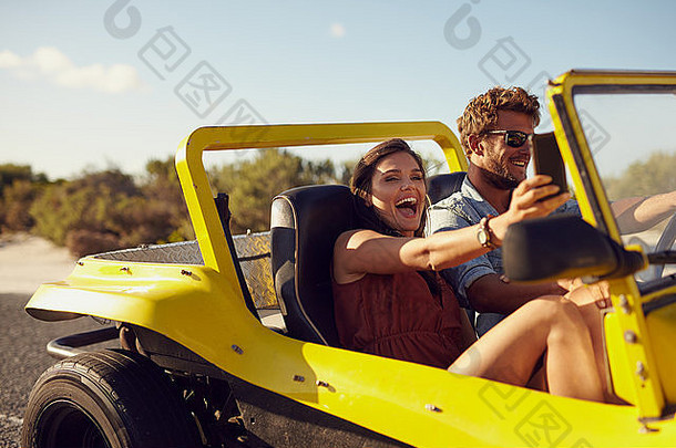 兴奋快乐夫妇享受路旅行车男人。开车车年轻的女人采取自拍移动电话