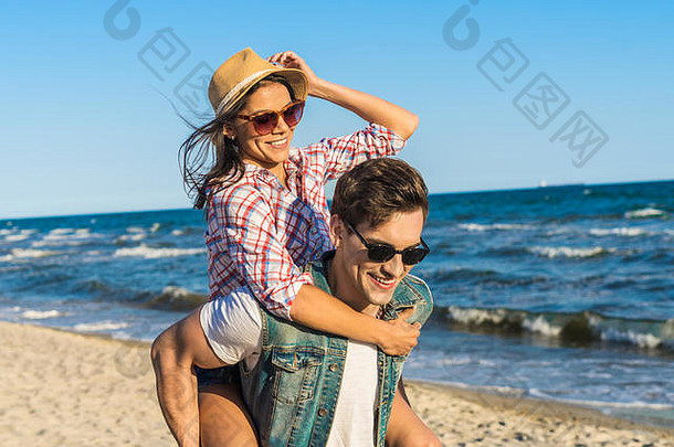 年轻的有趣的夫妇太阳镜肩扛海滩