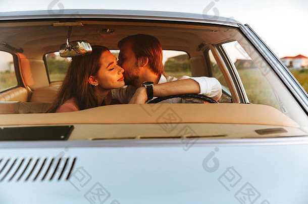 年轻的快乐夫妇接吻坐着内部车前面窗口视图