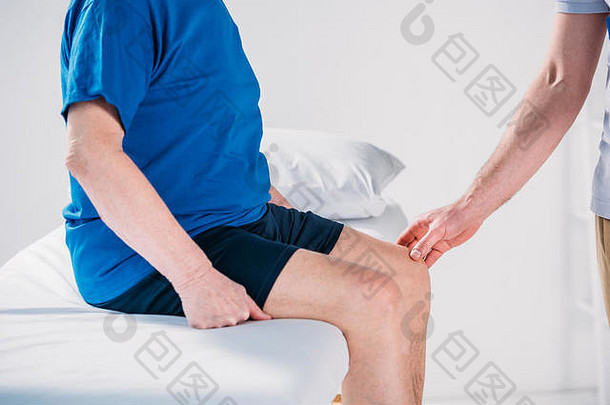 裁剪拍摄康复治疗师检查高级男人膝盖按摩表格