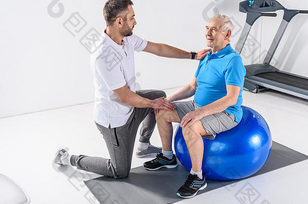 康复治疗师协助高级男人。锻炼健身球