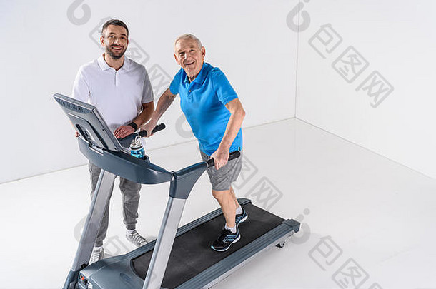 高角视图康复治疗师协助高级男人。锻炼跑步机