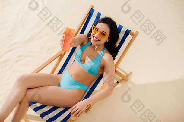 美丽的女孩太阳镜持有防晒霜瓶相机放松甲板椅子海滩
