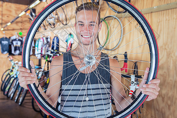 肖像微笑年轻的男人。持有自行车轮自行车商店