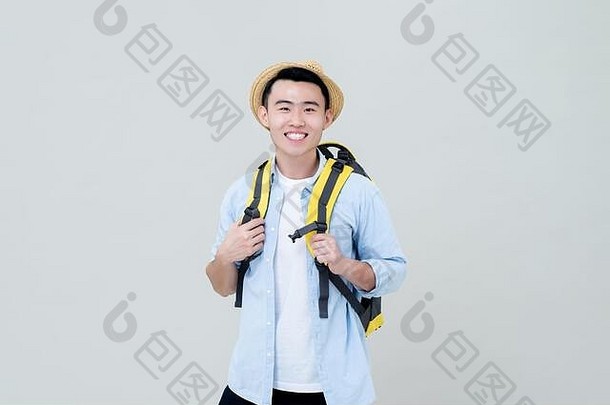 腰肖像年轻的微笑亚洲旅游男人。背包客持有黄色的背包肩带灰色的工作室背景