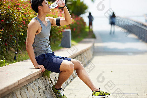 年轻的英俊的亚洲慢跑者采取打破喝水瓶一边视图
