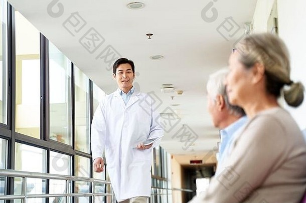 年轻的亚洲医生走医院走廊满足病人等待区域