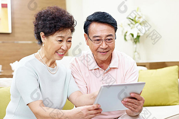 高级亚洲夫妇坐着沙发上平板电脑电脑快乐微笑