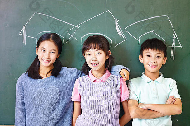 亚洲小学学校孩子们站下面chalk-drawn博士帽子前面黑板上