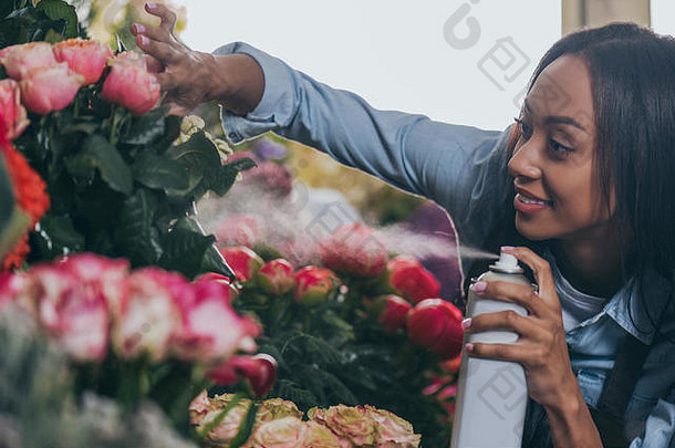 微笑年轻的非洲美国花店喷涂美丽的花