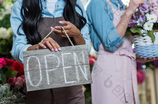 裁剪拍摄年轻的女人围裙持有开放标志站花商店