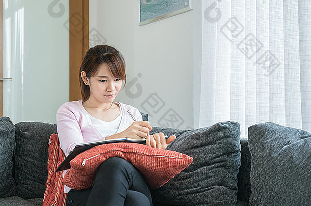 亚洲年轻的女人写作沙发上首页生活房间