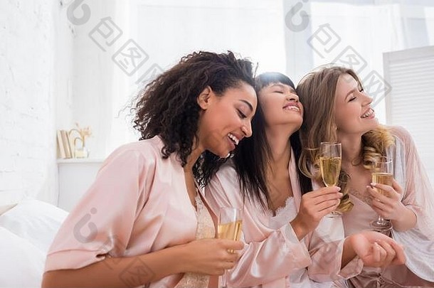 微笑多民族女朋友有趣的持有香槟眼镜睡衣聚会，派对