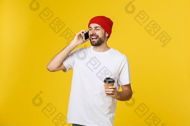 肖像快乐的年轻的男人。穿休闲衣服站孤立的黄色的背景持有移动电话喝