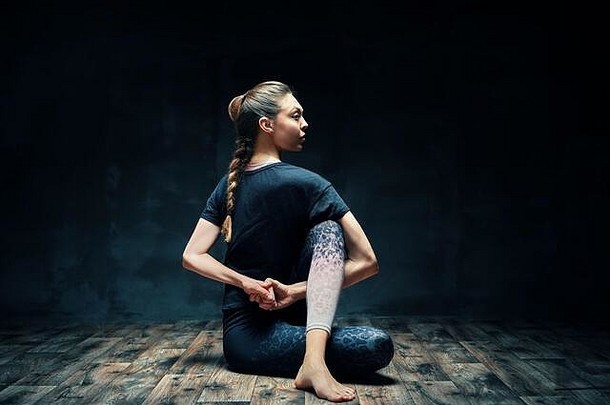 年轻的美丽的女人瑜伽体式一半主鱼构成黑暗房间