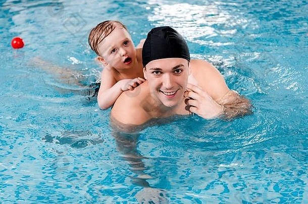 快乐游泳教练蹒跚学步的男孩培训游泳池