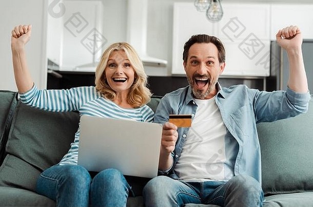 兴奋成熟的夫妇显示手势信贷卡移动PC沙发上