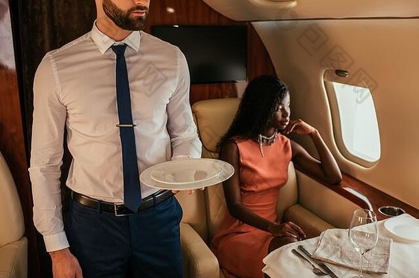 裁剪视图空气管家持有盘子沉思的非洲美国女人坐着服务表格飞机