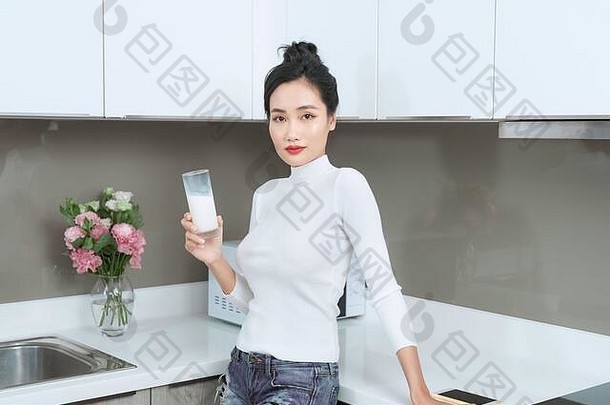 肖像年轻的女人站厨房喝牛奶