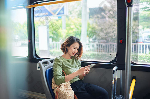 美丽的快乐年轻的女人坐着城市公共汽车移动电话