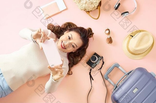 年轻的亚洲女人显示智能手机说谎粉红色的地板上旅行行李环绕前视图