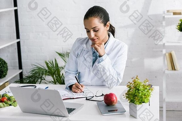有吸引力的女人白色外套写作笔记本移动PC蔬菜