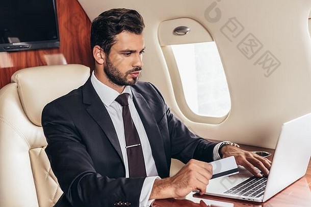 英俊的商人西装持有信贷卡移动PC私人飞机