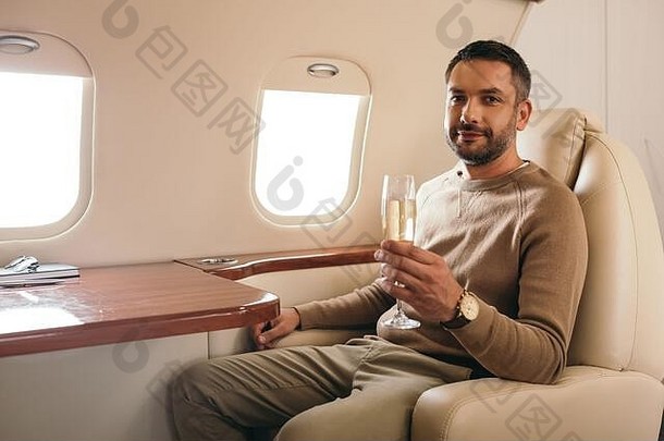 快乐的男人。持有香槟玻璃坐着类私人飞机