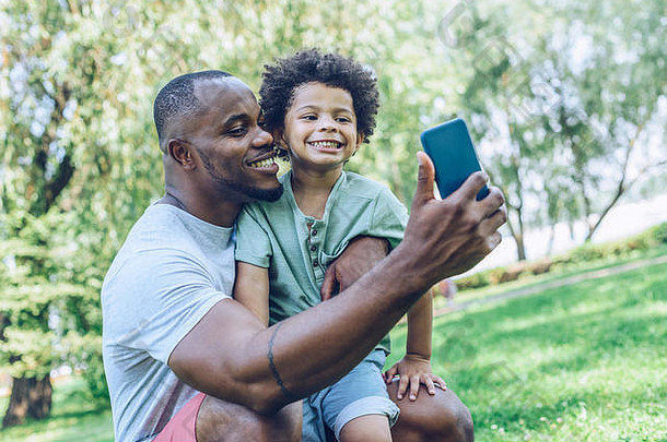 快乐非洲美国父亲儿子采取自拍智能手机公园