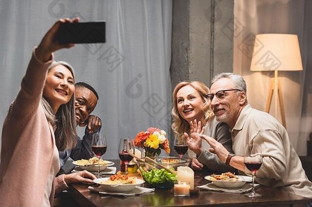 微笑多元文化的朋友采取自拍智能手机晚餐