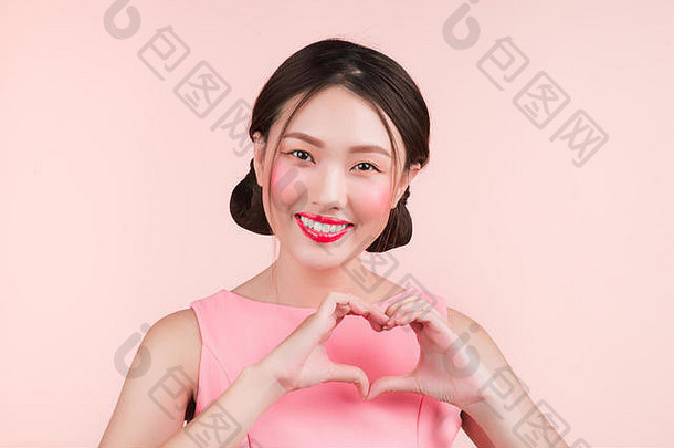 可爱的亚洲年轻的女人时尚化妆手势手使心形状孤立的粉红色的