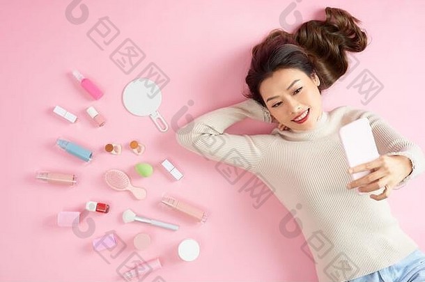 年轻的亚洲女人采取自拍电话说谎粉红色的背景化妆品前视图