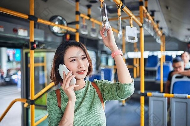 亚洲女人站城市公共汽车会说话的移动电话