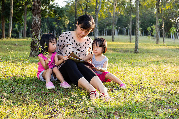 亚洲中国人妈妈。女儿阅读户外公园