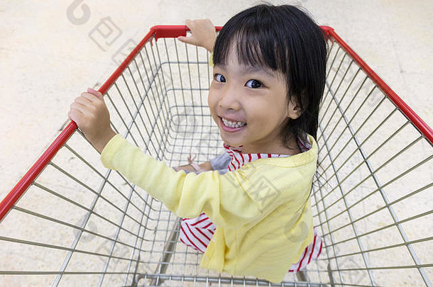 快乐亚洲中国人女孩坐着购物车超市