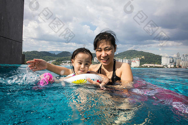 亚洲中国人妈妈。Daugther玩户外游泳池阳光明媚的一天
