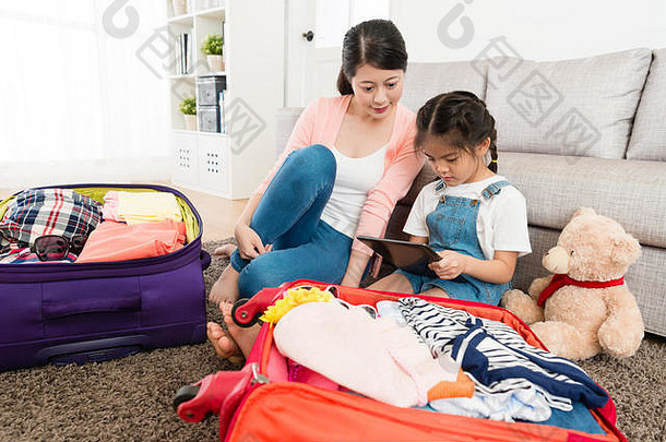 美丽的优雅的妈妈。女儿完成了包装行李移动数字平板电脑搜索旅行信息