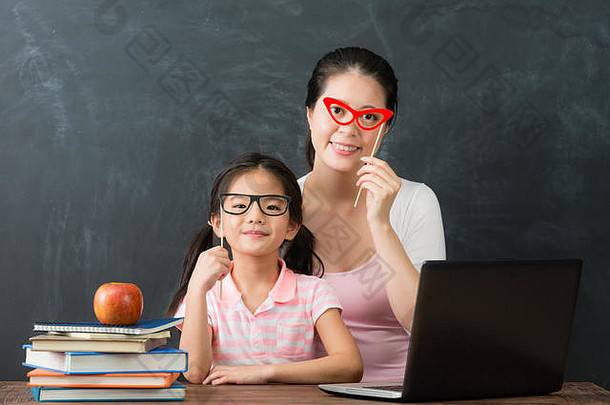 漂亮的年轻的妈妈。可爱的女儿研究电脑准备回来学校眼镜玩具衣服相机