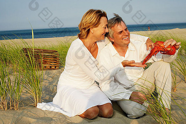 特写镜头成熟的男人。持有龙虾成熟的女人跪着海滩
