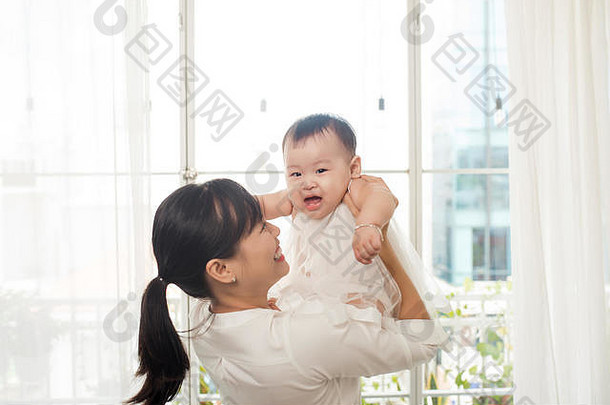 肖像快乐亚洲妈妈。婴儿有趣的首页白色房间窗口