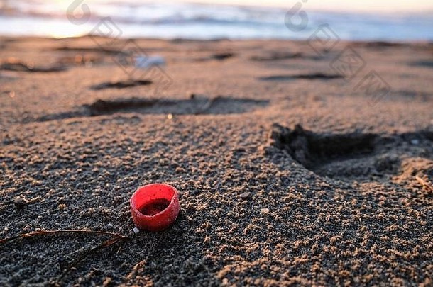 红色的塑料瓶软木塞日落海海岸被污染的生态系统塑料微粒