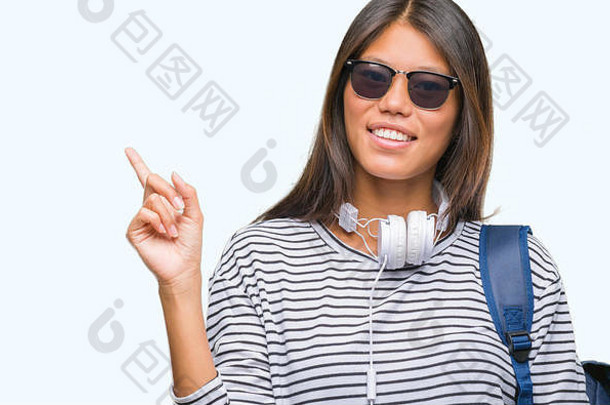 年轻的亚洲学生女人穿耳机背包孤立的背景<strong>大</strong>微笑脸指出手手指一边