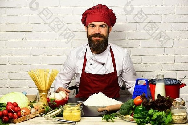 烹饪快乐脸统一的坐在表格蔬菜意大利面厨房用具专业烹饪概念老板准备餐男人。胡子坐成分白色砖墙背景