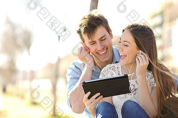 夫妇分享音乐唱歌平板电脑坐着板凳上城市公园