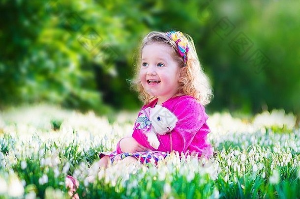 可爱的女孩可爱的卷曲的蹒跚学步的玩真正的兔子宠物兔子花园春天雪花莲花