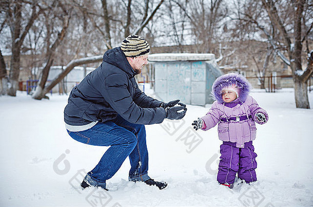 年轻的父亲女儿雕刻雪球冬天公园阳光明媚的一天